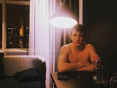 a shirtless man sitting at a table in front of a window next to a couch