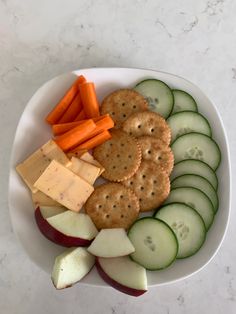 a white bowl filled with crackers, cucumbers and carrots