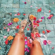 a woman's legs in water with flowers floating on the ground next to them