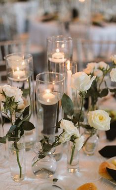 a table topped with lots of white flowers next to glasses filled with water and candles