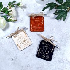 three tags tied with twine on top of a table next to flowers and leaves