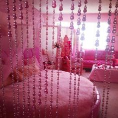 a pink bed sitting next to a window covered in beads