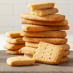 a stack of shortbread cookies sitting on top of a wooden cutting board next to a white brick wall