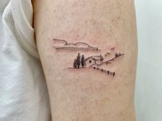 a person with a small tattoo on their arm that has a house and trees in the background