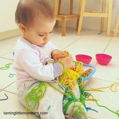 a toddler playing with some noodles on the floor