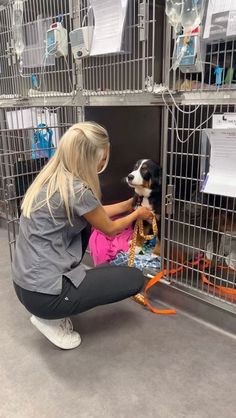 a woman kneeling down petting a dog in a cage