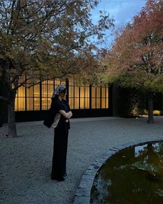 a woman standing in front of a pond with her arms crossed and looking off to the side