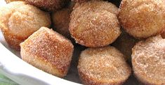 a white bowl filled with sugared muffins covered in powdered sugar and topped with a green leaf