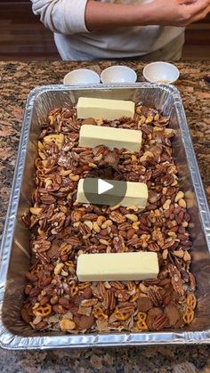 a person standing in front of a baking pan filled with granola, cheese and nuts