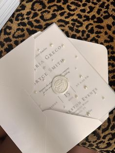 two white wedding cards on top of a leopard print table cloth with gold foil and pearls