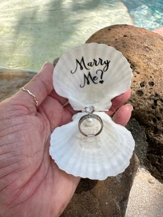 a person holding a shell with a wedding ring on it in front of a pool