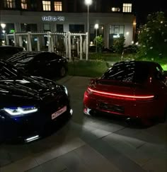 two cars parked next to each other in front of a building at night with lights on