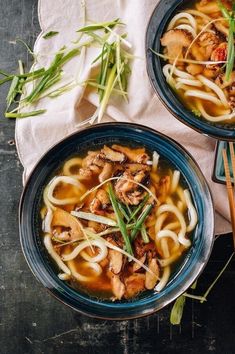 two bowls filled with noodles, meat and vegetables on top of a table next to chopsticks