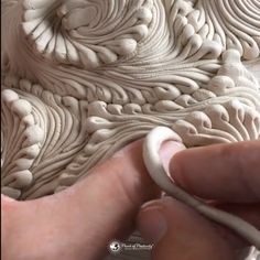 a person is working on an intricately designed object with white paint and wood shading