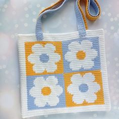 a crocheted flower bag hanging from a string on a white background with blue and yellow squares