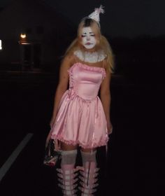 a girl in a pink dress and white face paint is standing on the street at night