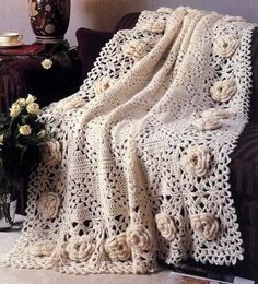 a white crocheted blanket sitting on top of a couch next to a vase with flowers