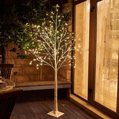 a lighted tree in front of a window on a wooden floor next to a bench