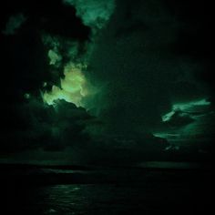 the sky is filled with clouds and green light in the dark night, as seen from an ocean shore