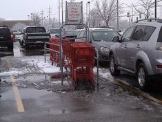 several cars parked in a parking lot with snow on the ground and behind them is a red shopping cart