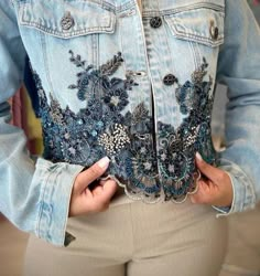 a woman wearing a jean jacket with blue flowers on the front and back, holding her hands in her pockets