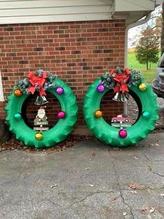 two green wreaths with decorations on them sitting in front of a brick building