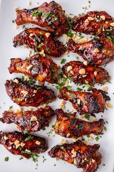 chicken wings covered in bbq sauce and garnished with chopped peanuts on a white plate