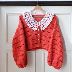 an orange crocheted sweater hanging on a door