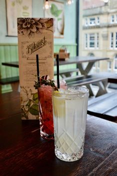 two drinks sitting on top of a wooden table next to a menu and some benches