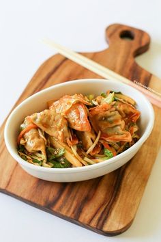 a white bowl filled with food on top of a wooden cutting board next to chopsticks