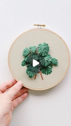 a person is holding a small embroidered plant in front of a white wall hanging on the wall