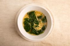 a white bowl filled with noodles and spinach on top of a cloth covered table