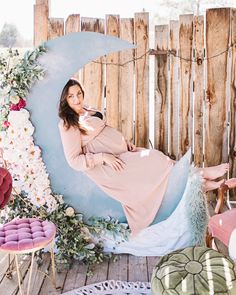 a pregnant woman sitting on the moon with flowers around her and posing for a photo