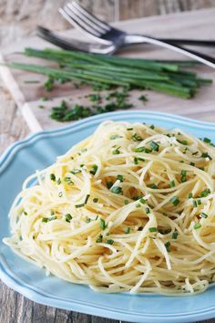 a blue plate topped with pasta and parsley on top of a wooden table next to a fork