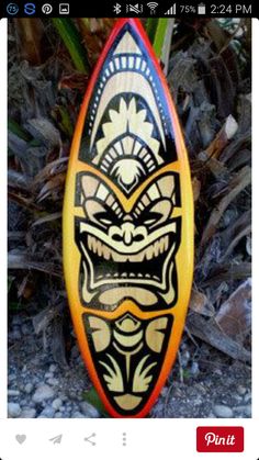 a colorful surfboard sitting on the ground next to some plants and rocks with an artistic design painted on it