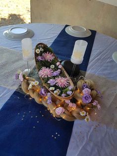 there is a flower arrangement in the middle of a table with candles and plates on it