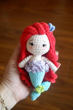 a crocheted little mermaid doll sitting on top of a wooden table next to a hand