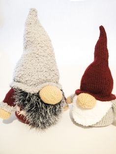 two knitted gnomes sitting next to each other on a white surface with one wearing a red hat