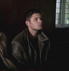 two young men sitting next to each other in a dark room with one looking off into the distance