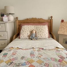 a bed with a quilt on it and a teddy bear sitting on top of it