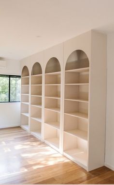 an empty room with white bookcases and wood floors in the foreground is a large window