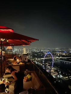 people are sitting at tables with umbrellas on top of a building overlooking the city