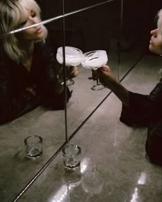 two women sitting on the floor looking at something in front of them with wine glasses