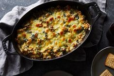 a casserole dish with cheese and spinach in it next to crackers