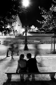 two people sitting on a bench in the middle of a park at night with their backs to each other