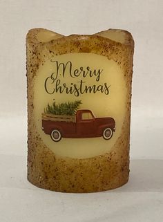 a lit candle with a red truck holding a christmas tree on it's back