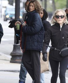 the woman is walking down the street talking on her cell phone and holding a cup