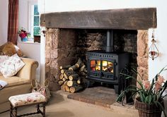 a wood burning stove in a living room next to a chair and fireplace with logs stacked on the floor