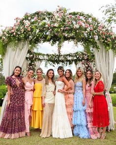 a group of women standing next to each other under a floral covered arch at a wedding