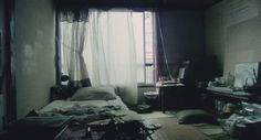 an unmade bed sitting next to a window in a room filled with clutter